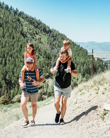 Two dads with kids on shoulders hiking a Wyoming mountain trail
